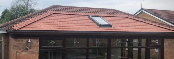 A single-storey extension with red roof tiles, a skylight window, and brown framed glass doors and windows, attached to a brick house.